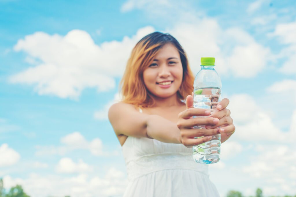 Women lifestyle concept young pretty woman wearing white dress with pick the Mineral Water bottle 