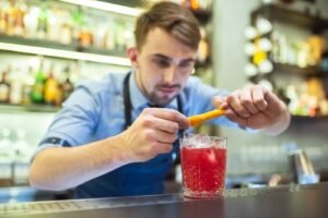 barman making red cocktail with orange bar