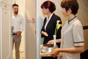 Manager and maid bringing tray with delicious dish as a compliment to smiling mature hotel guest