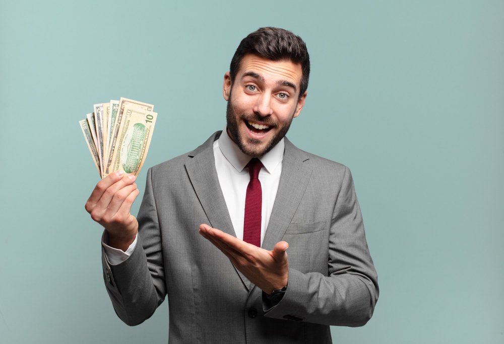 young-handsome-businessman-smiling-cheerfully-feeling-happy-showing-concept-copy-space-with palm-hand-bills-money