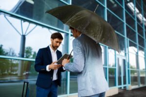 Two young businessmen talking at a rainy station
