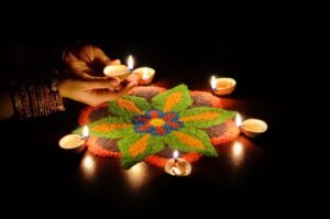 Cropped hands of woman holding diya over rangoli at night