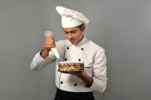 Happy male indian chef confectioner decorating chocolate cake
