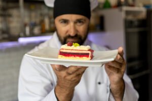 male chef in the kitchen holding plate of dessert