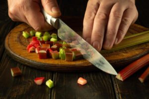 Closeup of a chef hands with a rhubarb slicing knife on a kitchen board